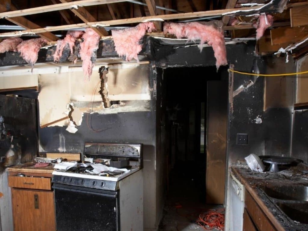 Kitchen interior coated in soot with exposed ceiling framing after fire damage