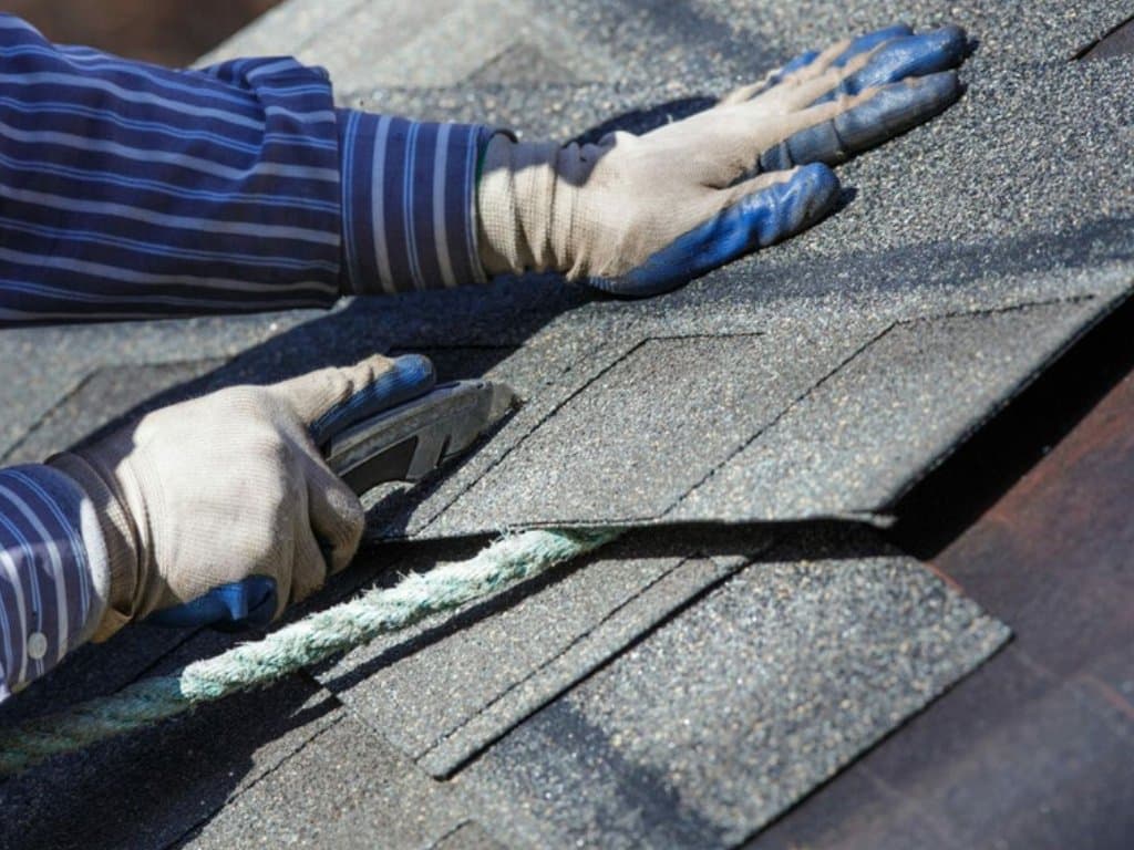 Public adjuster inspecting roof shingles by hand during a property damage assessment