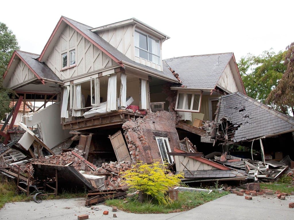 Two-storey home with a collapsed lower floor and brick debris after earthquake damage