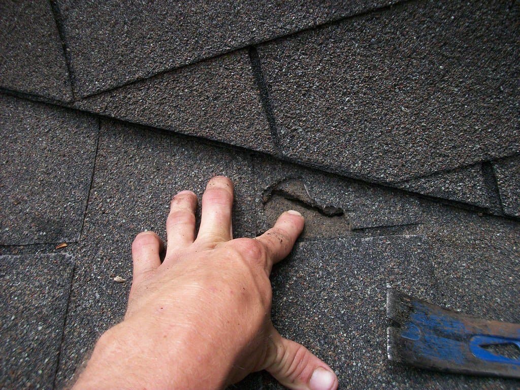 Hand inspecting a cracked asphalt shingle showing hail impact damage on a Texas roof